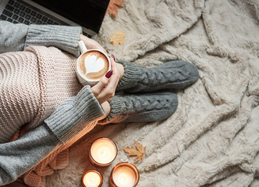 Cozy home, woman covered with warm blanket, drinks coffee.